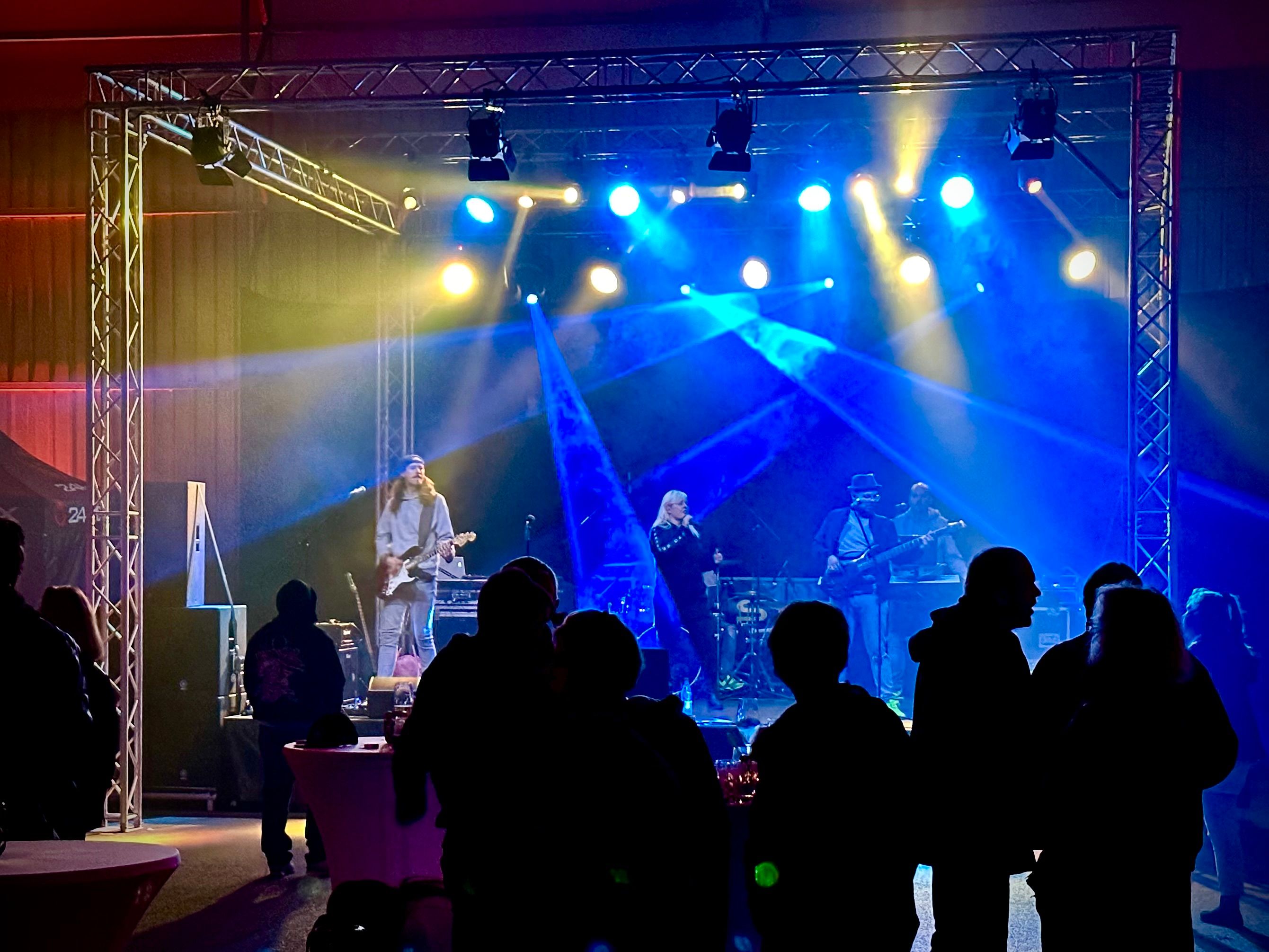 Bühne mit blauem Licht und Band, Publikum als Silhouette im Vordergrund