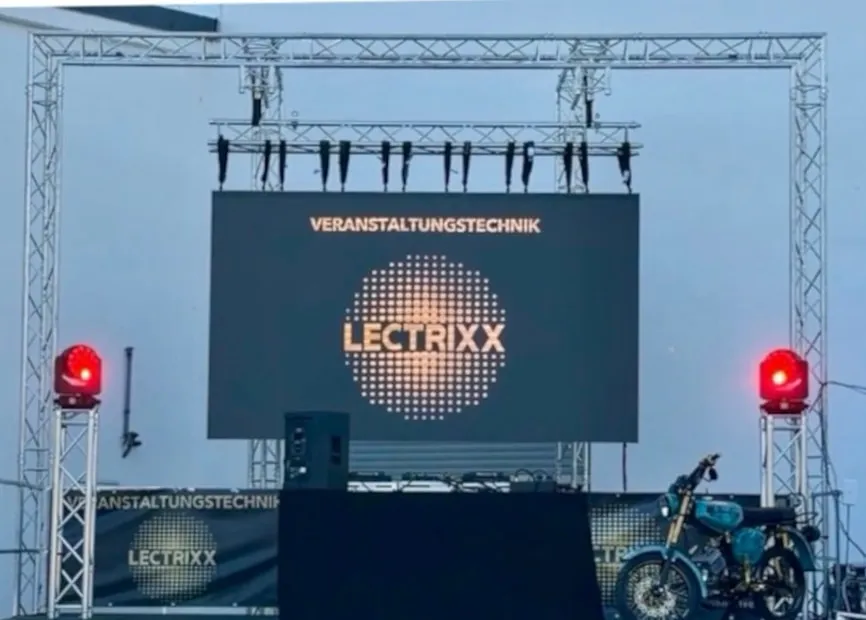 LED-Wand in einem Traversen-Rahmen mit dem LECTRIXX-Logo, darüber Scheinwerfer, seitlich zwei rote Moving Heads, davor ein DJ-Pult